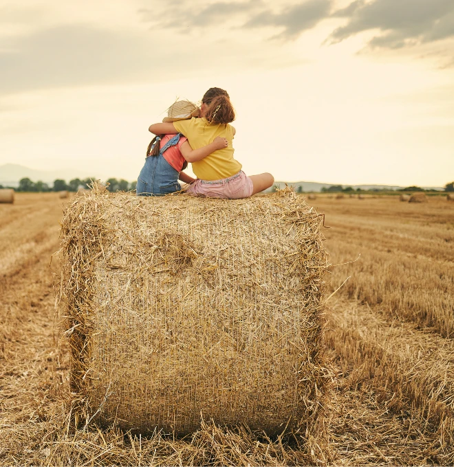 Let’s Start the Conversation Two girls sitting on a bale of haystack embraced and enjoying the view.
